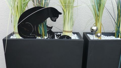 Schwarzer Pflanzencontainer aus Fiberglas mit Gras und Katzenmotiv im Vordergrund, im modernen Außenbereich platziert.