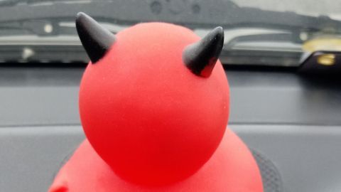Eine rote Gummikugel mit Teufelshörnern sitzt auf einer Antirutschmatte auf dem Armaturenbrett eines Autos.