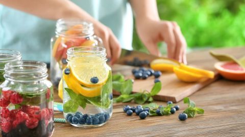 Glas mit frischer Zitrone und Blaubeeren wird zubereitet, während frische Früchte auf einem Holzbrett geschnitten werden.
