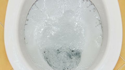 Eine Toilette mit sprudelndem Wasser, das Kalkablagerungen unter dem Rand entfernt, in einem hellen Badezimmer.