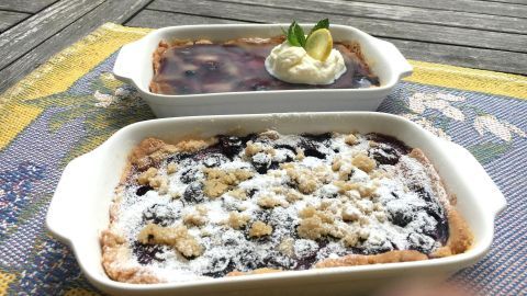 Zwei köstliche Schwedische Blaubeer-Tartelettes mit Pudding und Sahne liegen auf einem Holztisch im Sonnenschein.