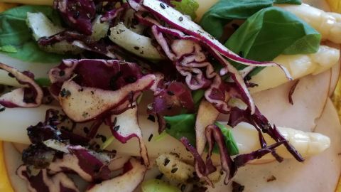 Eine bunte Kombination aus weißem Spargel und Rotkraut liegt auf zartem Putenbrustschinken in einer gelben Schale.