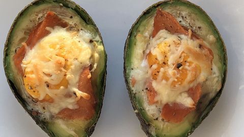 Zwei halbierte, gefüllte Avocados liegen auf einem weißen Teller, die mit Lachs und geschmolzenem Käse überbacken sind.