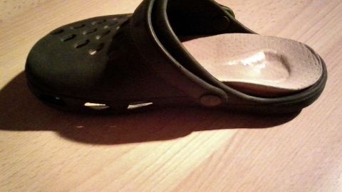 Ein Gummischuh liegt auf einem Holztisch, bereit für das Anbringen von Einlegesohlen zur besseren Passform.