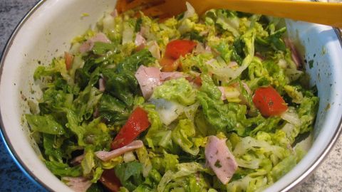Frischer Gemüse-Schinken-Salat wird mit gelben Besteck in einer Schüssel serviert, umgeben von einer modernen Küchendekoration.