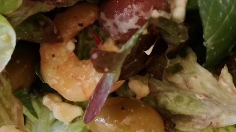 Frischer Pflücksalat mit Garnelen und Oliven liegt in einer Schüssel, umgeben von knackigem Gemüse und Dressing.