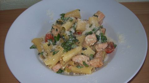 Rigatoni in einer weißen Schüssel, gemischt mit Kräutern und Sauce, serviert auf einem Holzuntergrund.