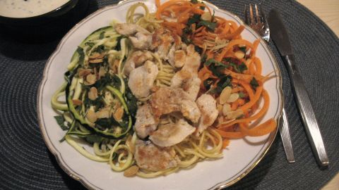 Bunter Spaghetti-Teller zeigt verschiedene Gemüsenudeln, die mit Hühnchen und Kräuter-Senf-Sauce dekoriert sind, auf einem Tisch.