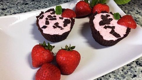 Zwei herzförmige Erdbeerdesserts mit Schokoladenstückchen und frischen Erdbeeren auf einem weißen Teller, umgeben von Grün.