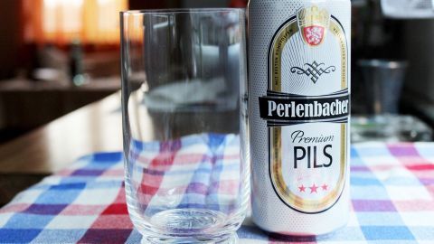 Ein Bierkrug steht neben einer leeren Glasflasche auf einem karierten Tischcloth, bereitet für ein frisches Pils.