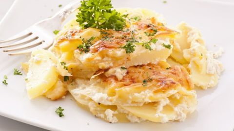 Ein goldbraunes Kartoffelgratin liegt auf einem weißen Teller, garniert mit frischer Petersilie und umgeben von feinen Kräutern.
