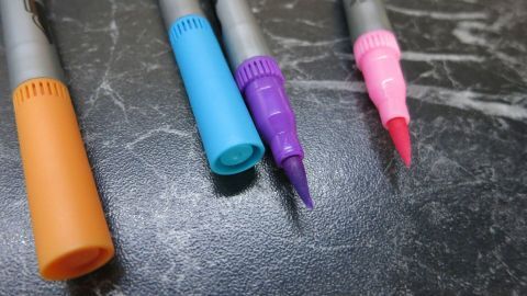 Mit einem Erfrischungstuch reibt man Filzstiftflecken im Teppichboden wunderbar heraus! Bunte Filzstifte liegen auf einer dunklen Oberfläche, bereit, um Flecken auf Teppichboden zu hinterlassen.
