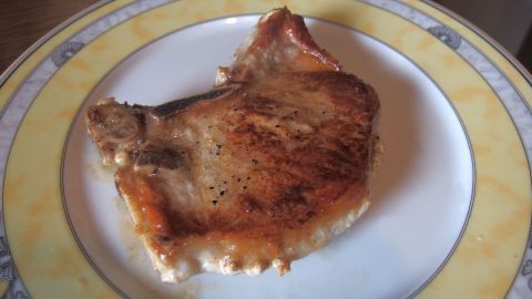 Ein Stück gebratenes Fleisch liegt auf einem weißen Teller mit gelbem Rand, bereit, warm gehalten zu werden.
