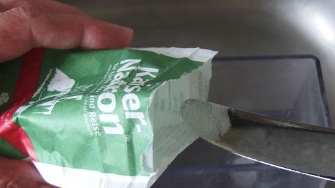 Ein grünes Päckchen wird mit einem Messer geöffnet, um möglicherweise Kaffee mit hartem Wasser zuzubereiten.