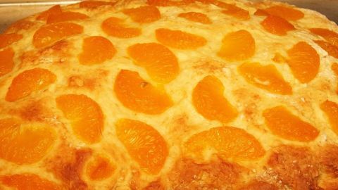 Ein Blechkuchen mit saftigen Mandarinenstücken ist goldbraun gebacken und liegt warm auf einem Blech.