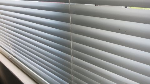 Jalousien sind in einem Fenster sichtbar, leicht schmutzig, und warten auf eine Reinigung mit SODA für frischen Glanz.
