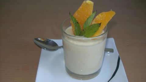 Ein Orangen-Dessert in einem Glas mit frischen Orangenscheiben und Minze, serviert auf einem weißen Teller.