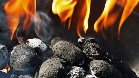 Schwarze Grillkohlen brennen, während Flammen aufsteigen, und zeigen eine alternative Methode, um Nachos anzuzünden.