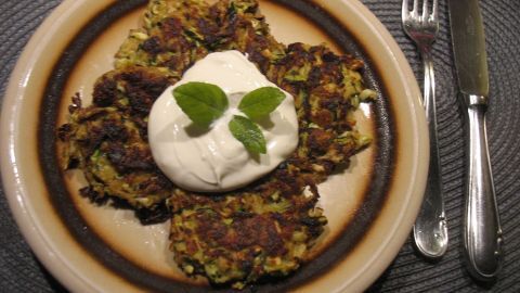Knusprige Zucchini-Rösti liegen auf einem Teller, garniert mit einem Klecks Sahne und frischen Minzblättern.