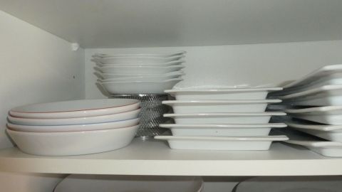 Geschirr ist im Küchenschrank ordentlich gestapelt, um platzsparend untergebracht zu werden, dabei sind verschiedene Teller und Schalen sichtbar.