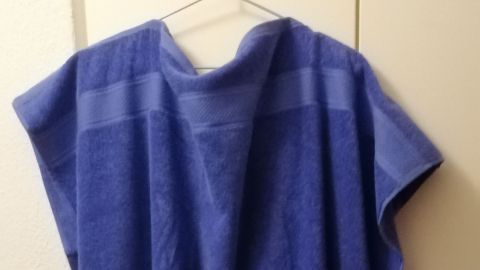 Ein blaues Badeüberziehkleid aus Duschtüchern hängt an einer Wand und zeigt die einfache, praktische Form.