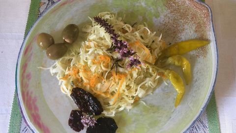 Ein frisch zubereiteter Krautsalat liegt auf einem Teller, umgeben von grünen Oliven und gelben Paprikastreifen.