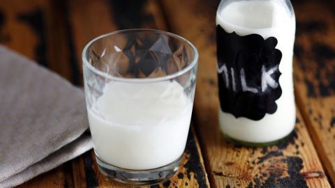 Ein Glas Milch steht neben einer Flasche mit der Aufschrift „MILK“ auf einer rustikalen Holzoberfläche.