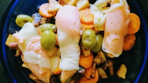 Auf einem blauen Teller liegen bunte Gemüsestücke wie Karotten und Oliven, garniert mit Lachs-Käse-Röllchen.
