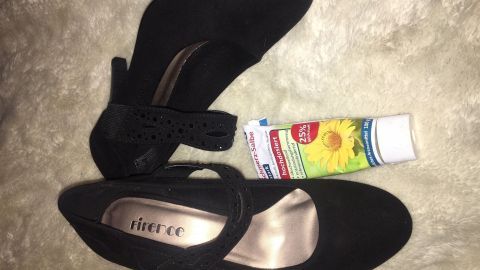 Schwarze High Heels liegen neben einer Tube Fußcreme auf einem weichen, hellen Untergrund, bereit für Linderung nach dem Tanzen.