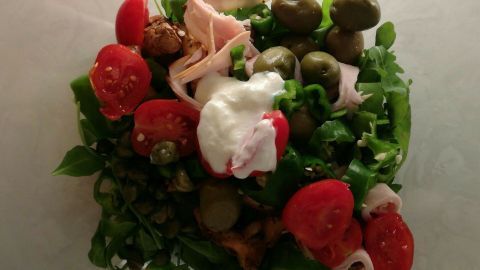 Frischer Rucola-Salat wird mit Kirschtomaten, Pfifferlingen und Putenschinken in einer Schüssel angerichtet.