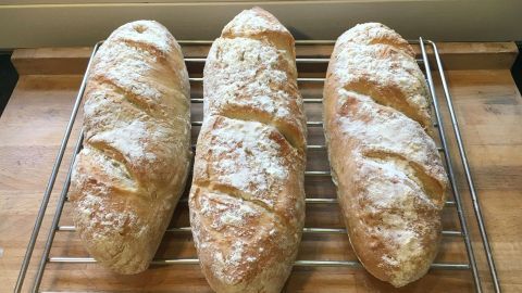 Drei frisch gebackene Baguettes ruhen auf einem Gitterrost in einer hellen Küche, bereit zum Servieren.