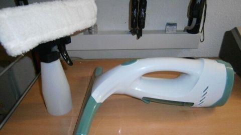 Ein Akku-Fensterreiniger liegt neben einem Sprühbehälter auf einem Tisch, bereit für die Reinigung von Fenstern.