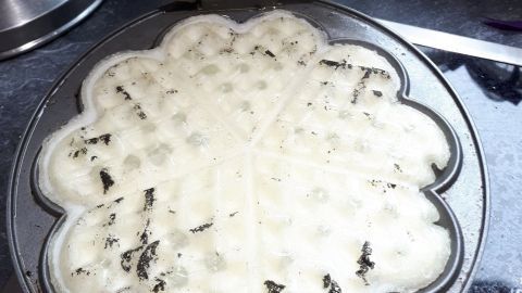 Ein Waffeleisen mit angebackenem Teig steht geöffnet auf einer Arbeitsfläche, bereit zur Reinigung mit Speisestärke.