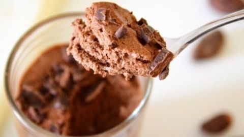 Eine Löffelportion Mousse au Chocolat hebt sich über einem Glas, umgeben von Schokoladenstückchen auf einem hellen Hintergrund.