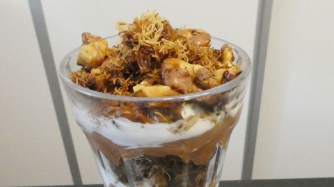 Ein Glas Dessert ist gefüllt mit Schichten aus Schokoladencreme und Engelnhaar, dekoriert mit knusprigen Nüssen.