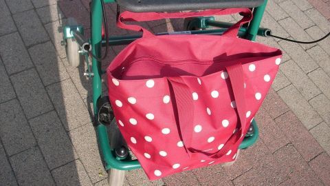 Eine rote Punktetasche hängt an einem Standard-Rollator, bereit, persönliche Gegenstände bequem zu transportieren.