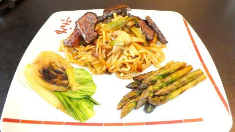 Saftiges Steak Teriyaki liegt auf einem weißen Teller, umgeben von Pak Choi und grünem Spargel in einer asiatischen Anrichtung.