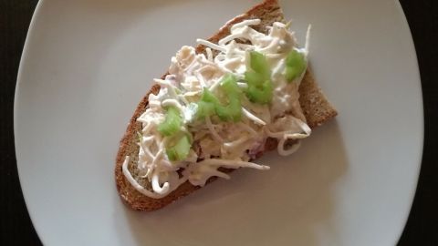 Ein belegtes Brot liegt auf einem weißen Teller. Es ist mit einer cremigen Räucherforellenpaste und frischen Sojasprossen sowie Stangensellerie belegt.
