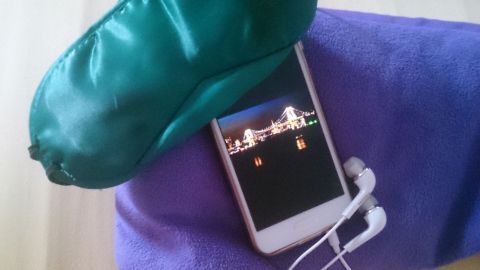 Ein Smartphone mit Kopfhörern zeigt eine beruhigende Meditationsszene, während eine Schlafmaske auf einem weichen Tuch liegt.