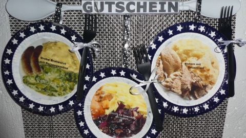 Ein Gutschein hängt über Tellern mit verschiedenen Mahlzeiten, um Senioren eine Zeit- und Mahlzeiterfahrung zu schenken.