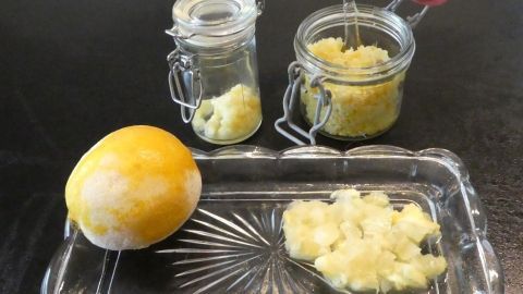 Gelbe Zitrone und Gläser mit gefrorenem Zitronenpüree liegen auf einem klaren Teller, bereit zur Verwendung in der Küche.