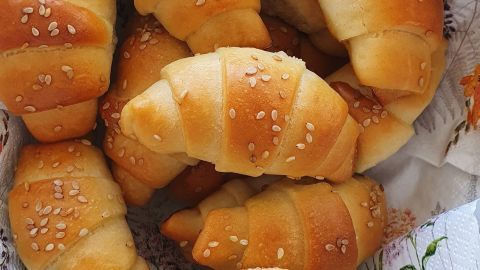 Zarte Croissants, frisch gebacken, liegen auf einem dekorativen Tuch in einem weißen Korb.