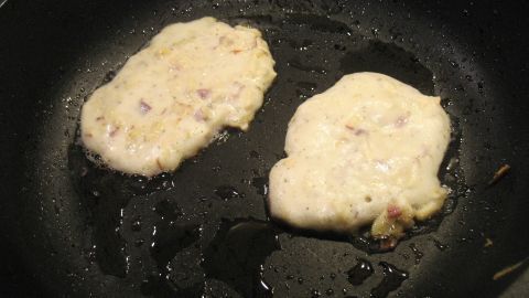 Zwei luftige Eierkuchen bräunen in einer Pfanne, umgeben von heißem Öl, mit Apfel und Schinken zubereitet.