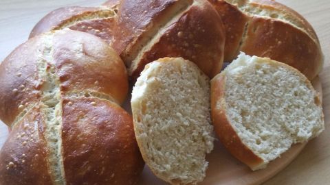 Zarte Brötchen mit knuspriger Kruste liegen auf einem Holzbrett, eines davon ist in der Mitte aufgeschnitten.