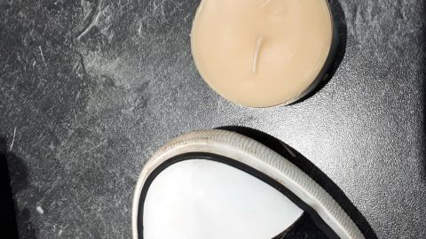 Die Turnschuhe mit weißen Kappen stehen auf einem dunklen Untergrund neben einer schützenden Creme, die sie vor Schmutz bewahrt.