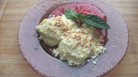 Zwei Portionen weiße Mousse au Chocolat liegen auf einem runden, lila Teller, garniert mit Minze und einer Fruchtsoße.