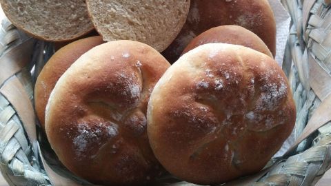 Ein Korb mit frisch gebackenen Dinkel-Buttermilch Brötchen liegt auf einem Tisch, einige sind halbiert.