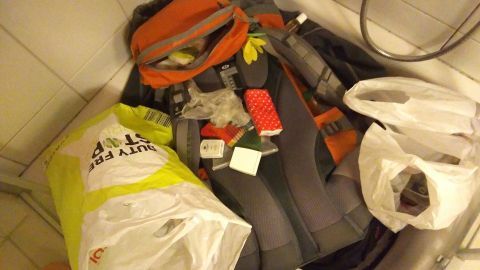 Ein schwarz-grau-orangefarbener Rucksack und zwei Tüten liegen in einer Badewanne, möglicherweise nach einem Urlaub.