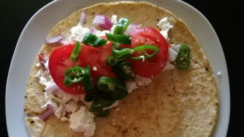 Ein Pfannkuchen wird gefüllt mit Schafskäse, Tomaten und Grillpaprika auf einem weißen Teller präsentiert.