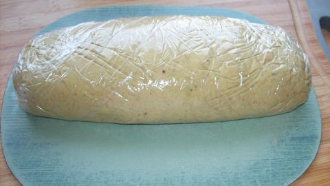 Die Pilzbutter ist als länglicher, in Frischhaltefolie gewickelter Block auf einer blauen Unterlage zu sehen.